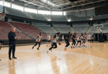 Basketball players participating in professional tryouts on indoor court with coaches evaluating