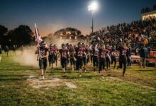 High school football team taking the field for evening game under stadium lights
