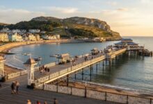 Victorian pier extending into coastal waters with historic tramway on hillside in background